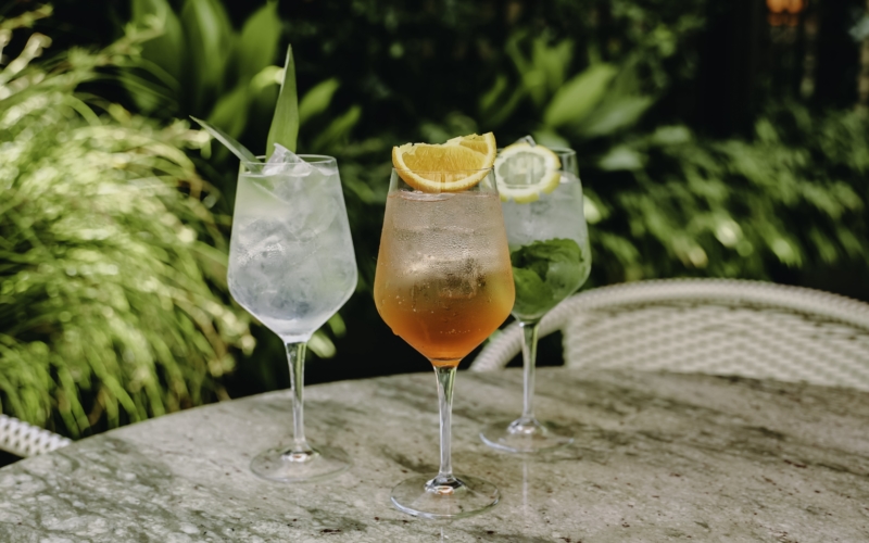 three cocktails on a marble table with greenery in background
