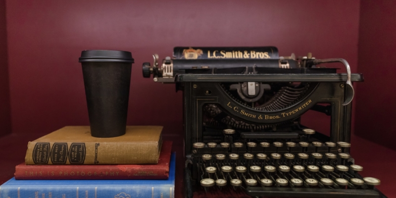 Coffee cup on top of a stack of books, next to a typewriter
