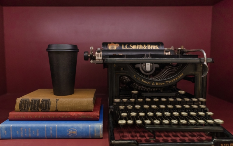 Coffee cup on top of a stack of books, next to a typewriter