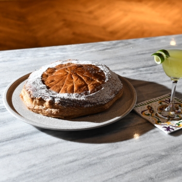 Round pastry on a plate next to a yellow-green cocktail