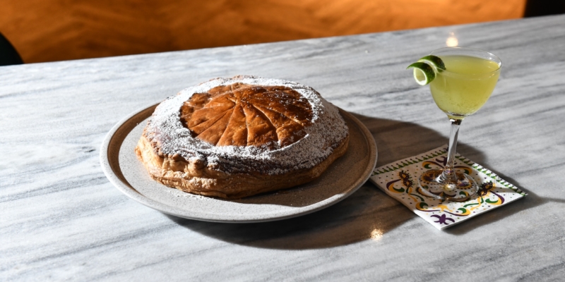 Round pastry on a plate next to a yellow-green cocktail